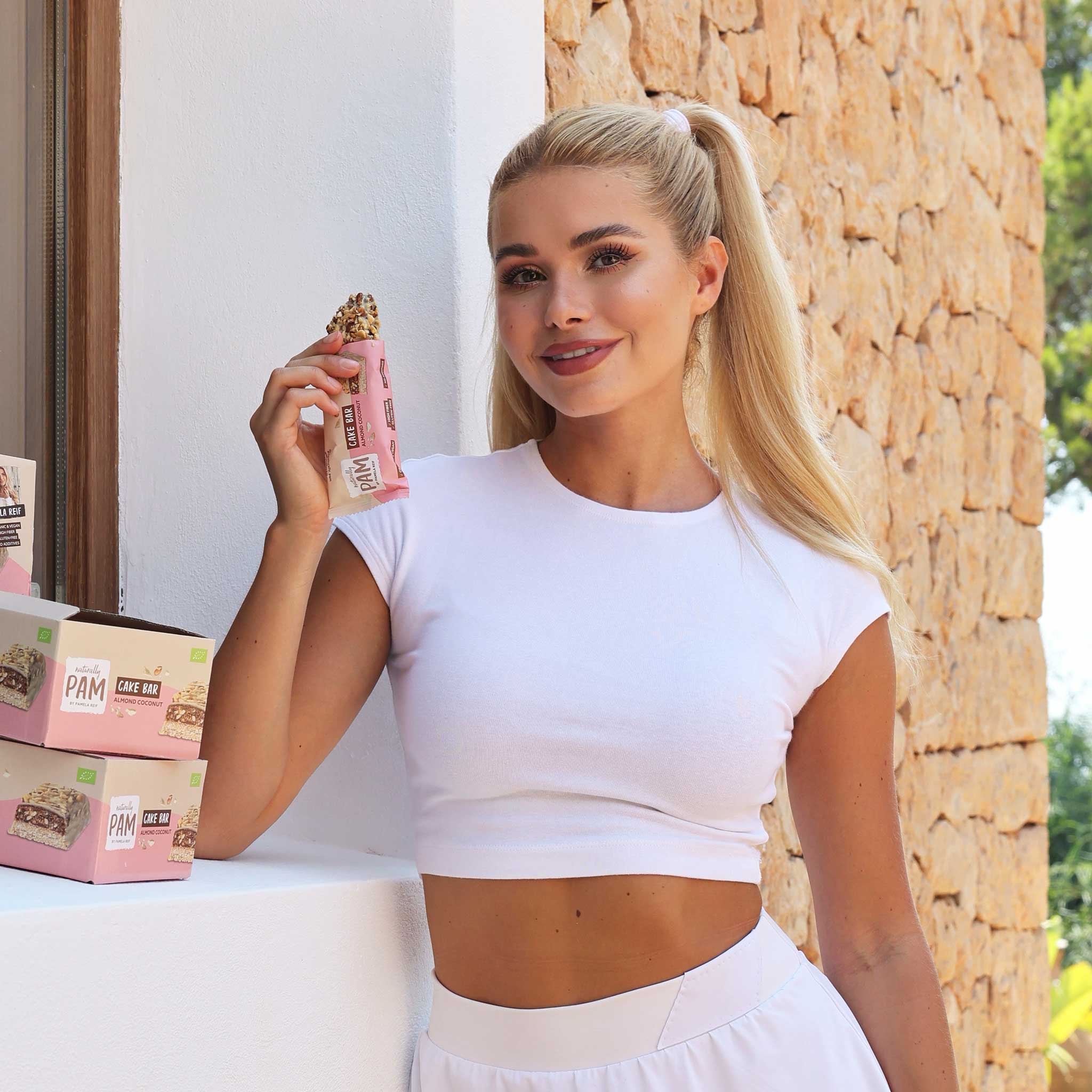 Naturally Pam Cake Bar mit Mandeln und Kokosnuss, zeigt die Riegel mit Nüssen und Kokosstücken auf der Verpackung